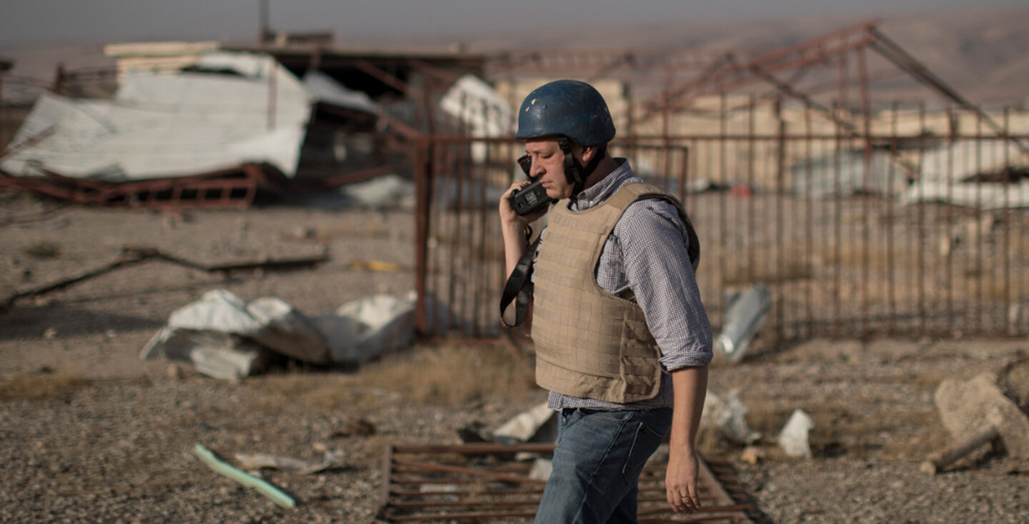 A photographer carrying a camera  wearing a helmet and flak jacket