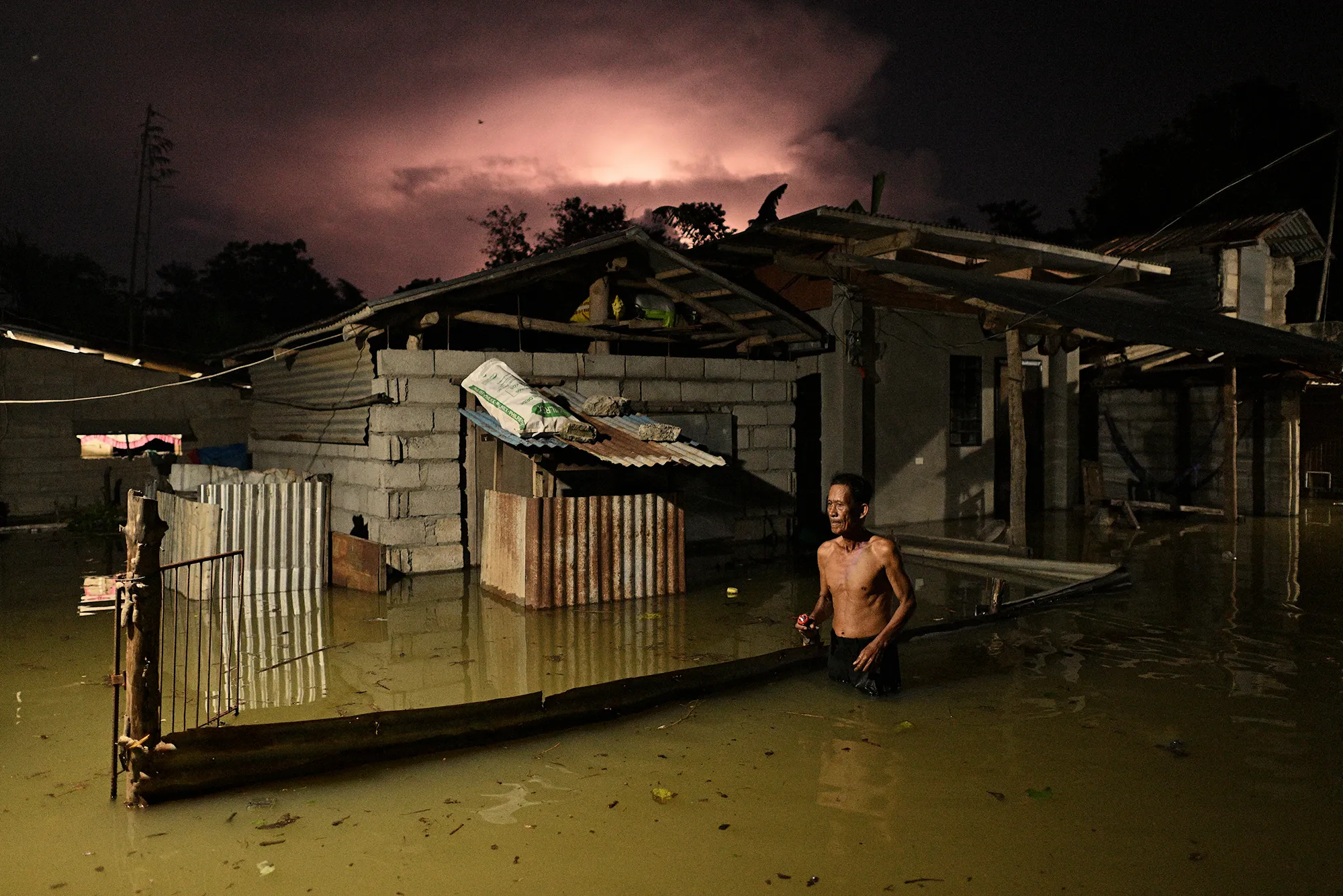 Man walking through flood water  in front of a flooded house